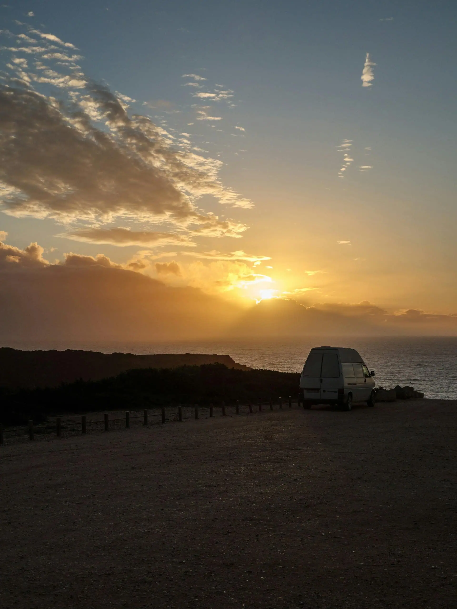 A campervan parked at a scenic coastline at sunset